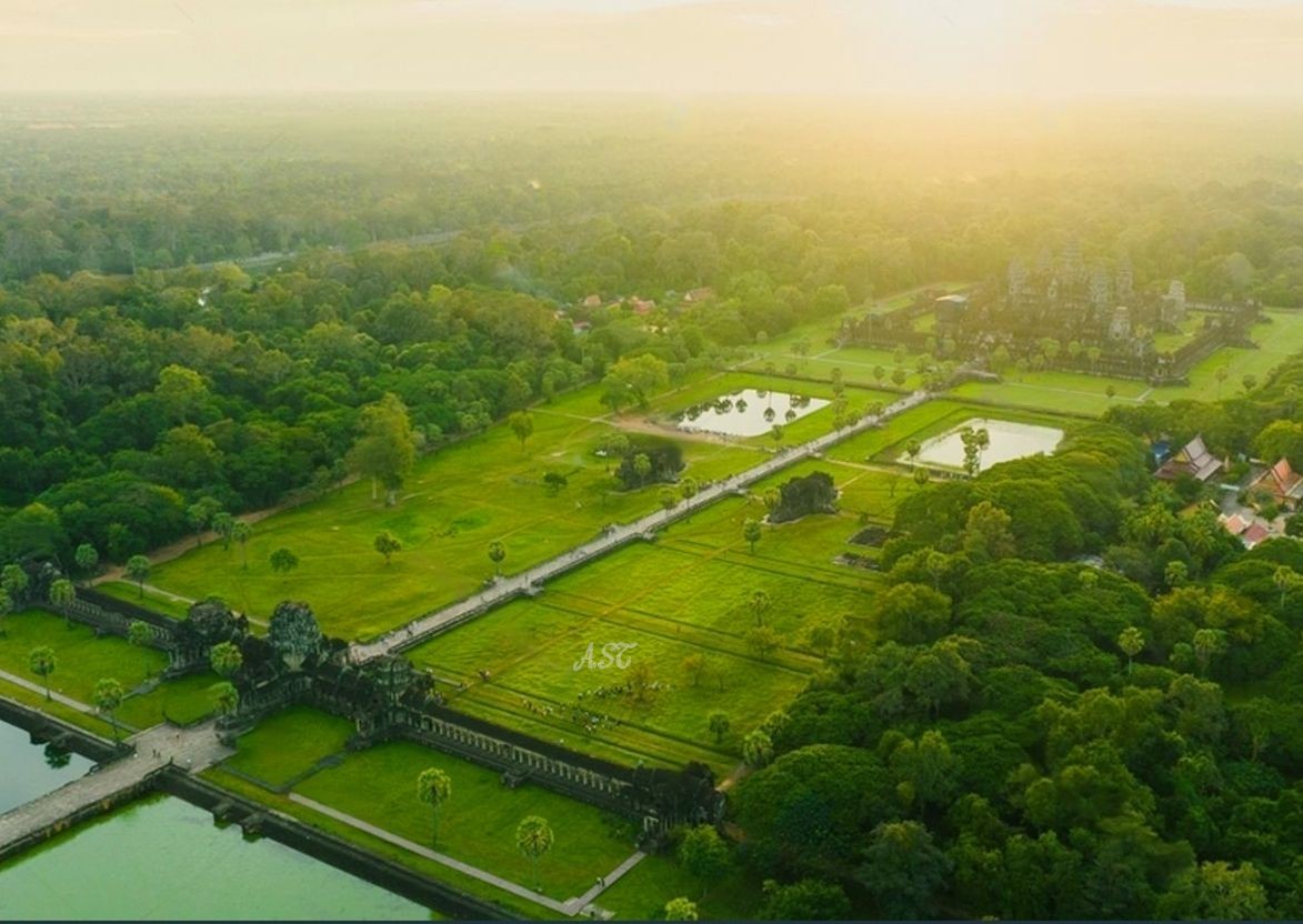 Aerial view of ancient ruins surrounded by lush greenery and ponds at sunrise.